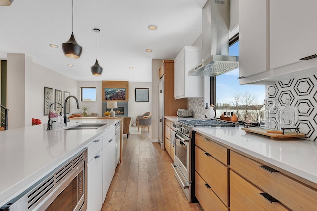 kitchen featuring appliances with stainless steel finishes, decorative light fixtures, white cabinetry, sink, and island range hood