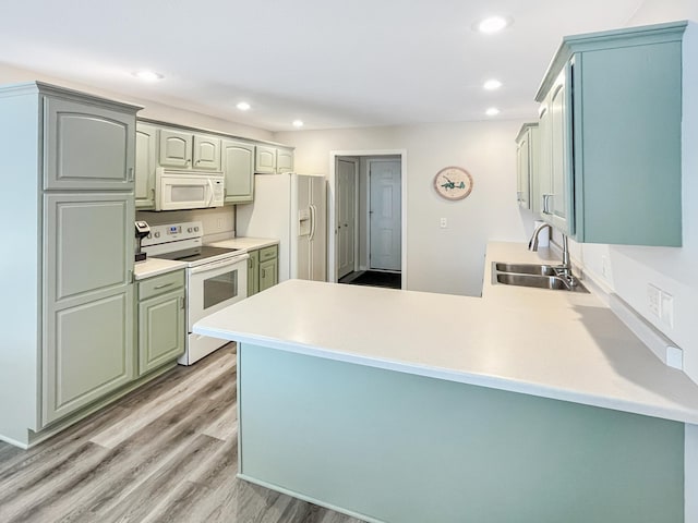 kitchen featuring white appliances, kitchen peninsula, sink, and light wood-type flooring