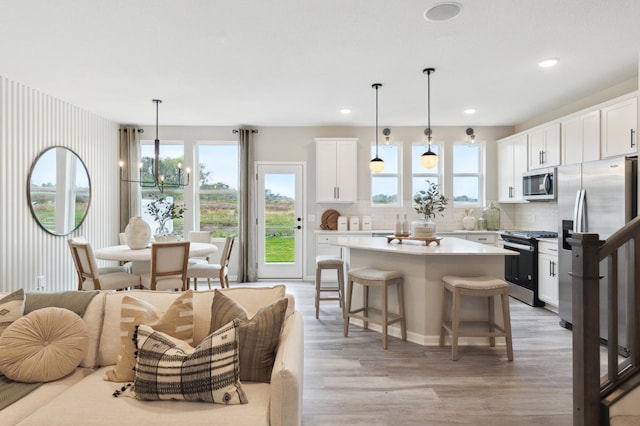 kitchen featuring appliances with stainless steel finishes, hanging light fixtures, decorative backsplash, white cabinets, and a kitchen island