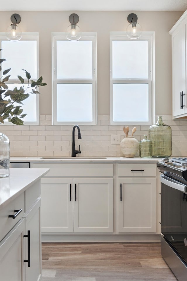 kitchen with decorative light fixtures, white cabinetry, sink, backsplash, and stainless steel range with electric stovetop