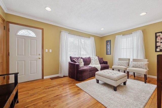 living room with light wood finished floors, a textured ceiling, crown molding, and baseboards