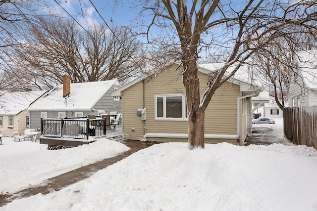 snow covered rear of property featuring a deck and fence