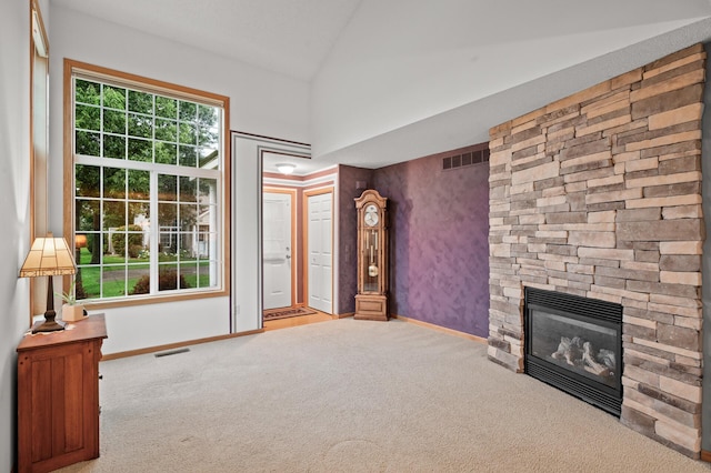 unfurnished living room featuring vaulted ceiling, a stone fireplace, and light colored carpet