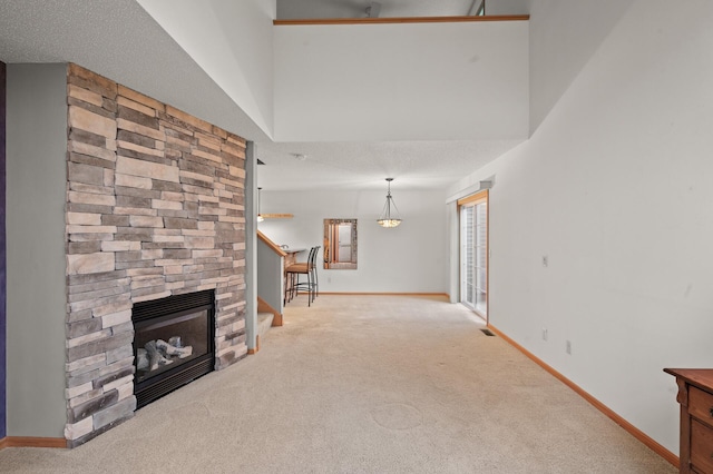 unfurnished living room featuring light colored carpet, a textured ceiling, and a stone fireplace