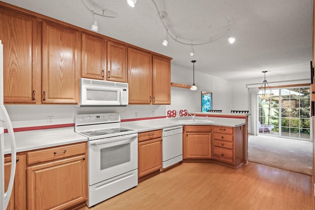 kitchen featuring kitchen peninsula, light hardwood / wood-style flooring, decorative light fixtures, sink, and white appliances