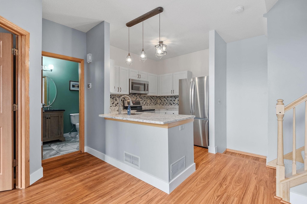 kitchen with stainless steel appliances, white cabinets, decorative light fixtures, kitchen peninsula, and light wood-type flooring