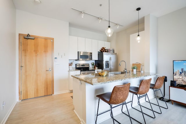 kitchen with pendant lighting, white cabinets, stainless steel appliances, light hardwood / wood-style floors, and sink