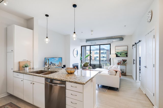 kitchen featuring a barn door, stainless steel dishwasher, white cabinets, decorative light fixtures, and sink