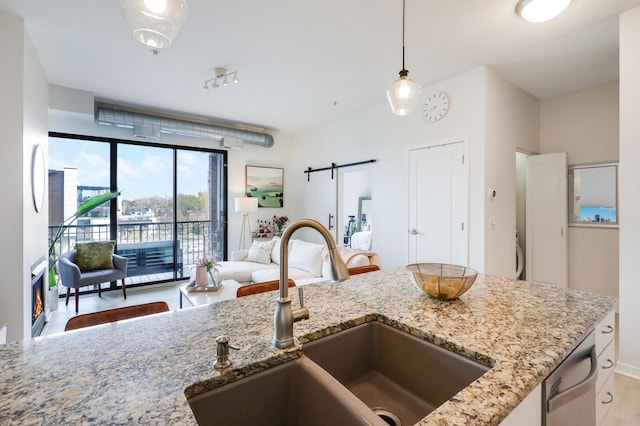 kitchen with sink, decorative light fixtures, a barn door, and light stone countertops