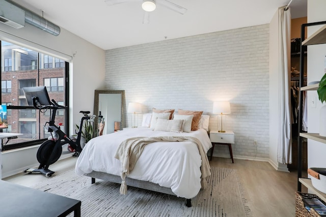 bedroom with ceiling fan, brick wall, and light hardwood / wood-style flooring