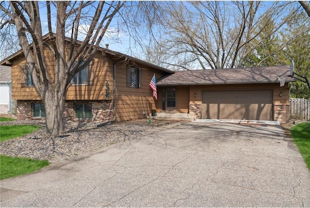 tri-level home featuring brick siding, driveway, a garage, and fence