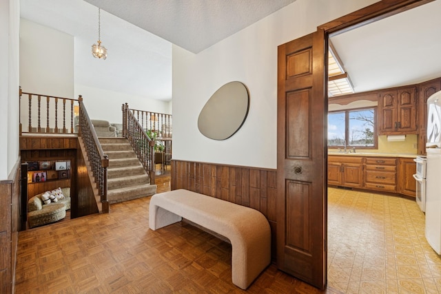 interior space with a textured ceiling, wood walls, wainscoting, light floors, and stairs