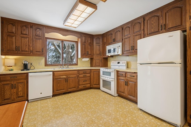 kitchen with brown cabinetry, white appliances, light countertops, and a sink