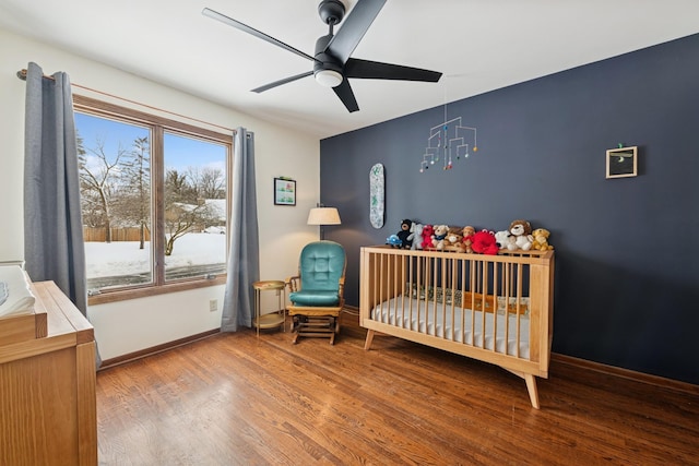 bedroom featuring a nursery area, wood finished floors, baseboards, and ceiling fan