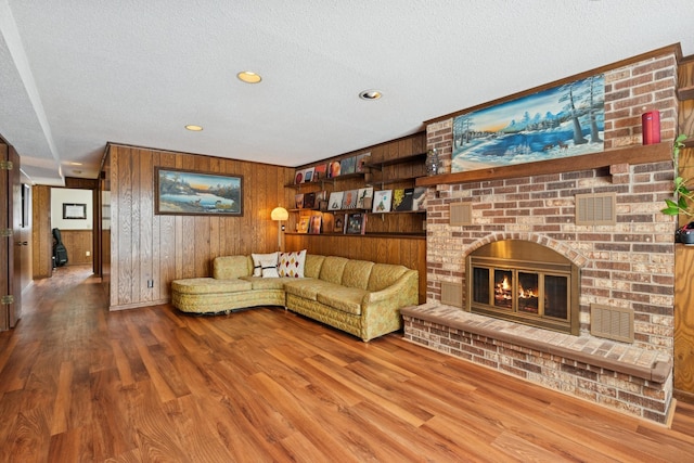 living area featuring visible vents, a brick fireplace, wood walls, wood finished floors, and a textured ceiling