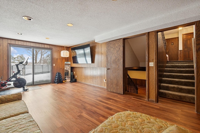 living room with wooden walls, a textured ceiling, stairs, and wood finished floors