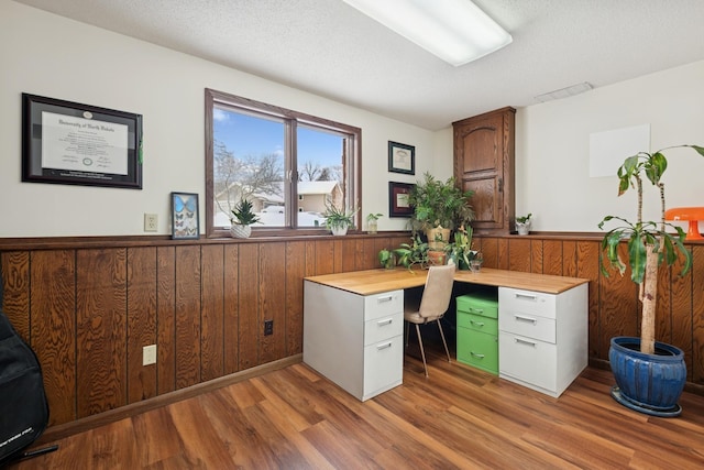 unfurnished office featuring light wood finished floors, wooden walls, visible vents, wainscoting, and a textured ceiling