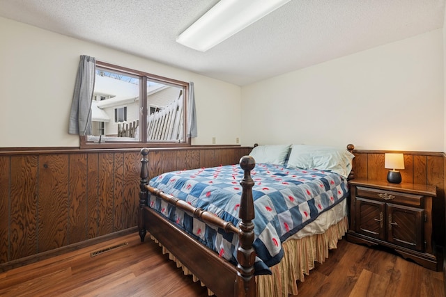 bedroom featuring visible vents, wainscoting, wooden walls, and wood finished floors