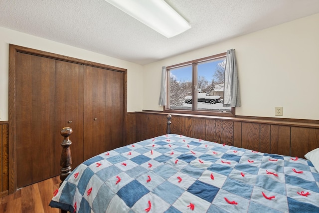 bedroom with a textured ceiling, wood finished floors, wainscoting, and wood walls