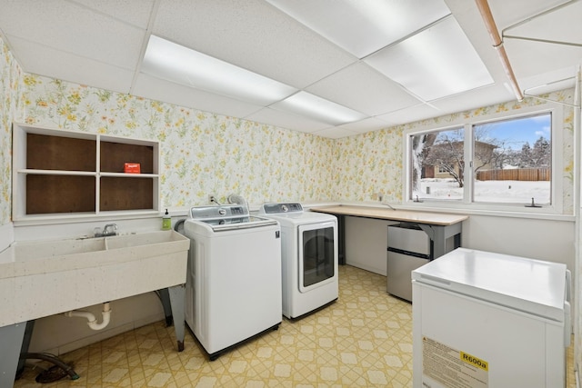 clothes washing area with washing machine and dryer, light floors, wallpapered walls, and laundry area