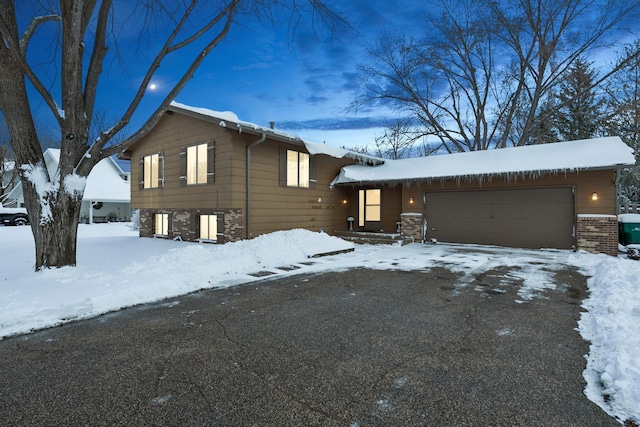 split level home featuring stone siding, an attached garage, and driveway