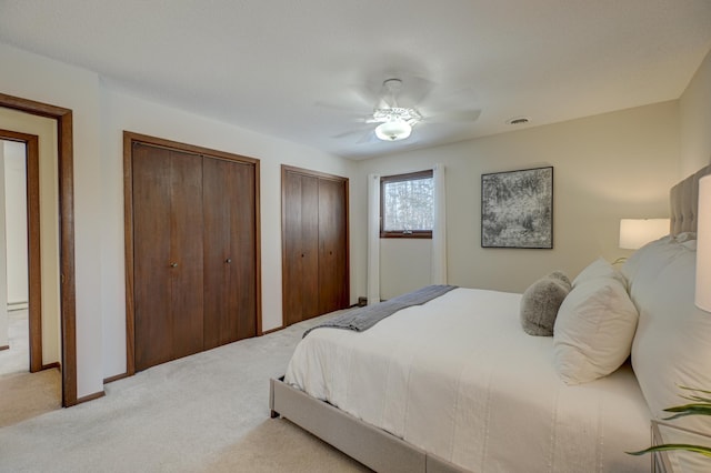 bedroom with ceiling fan, light colored carpet, and two closets