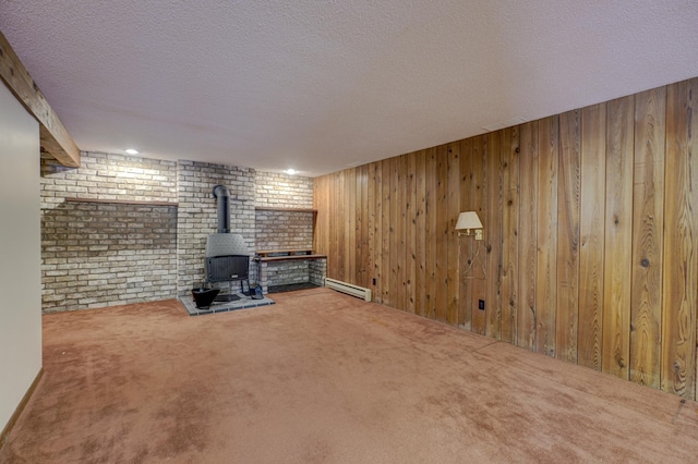 basement featuring a wood stove, carpet floors, a baseboard heating unit, a textured ceiling, and wooden walls