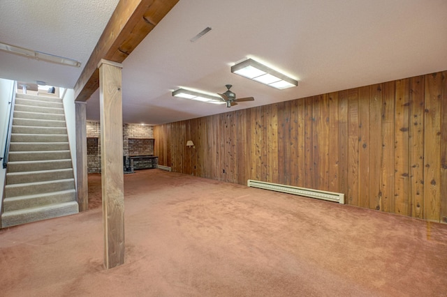 basement featuring carpet, a brick fireplace, wood walls, baseboard heating, and ceiling fan