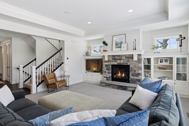 carpeted living room featuring crown molding, a fireplace, a raised ceiling, stairway, and baseboards