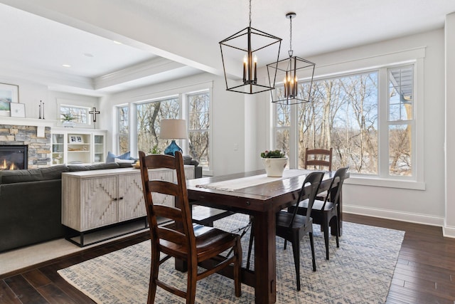 dining area featuring baseboards, dark wood finished floors, a tray ceiling, and a stone fireplace