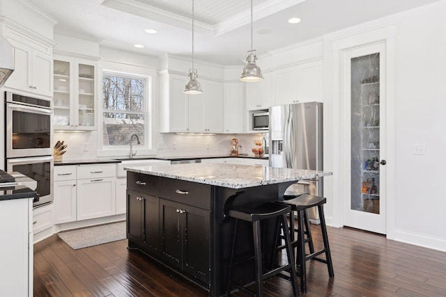 kitchen with white cabinets, a raised ceiling, a kitchen island, appliances with stainless steel finishes, and ornamental molding