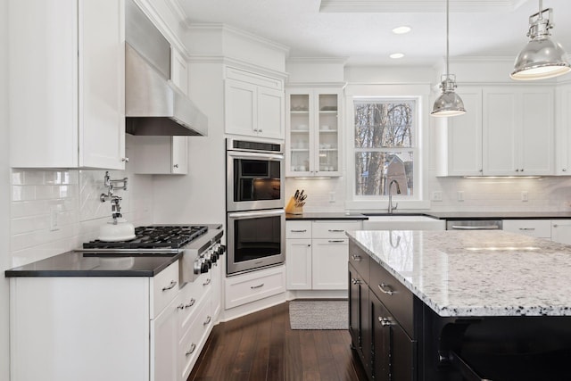 kitchen with a sink, white cabinetry, appliances with stainless steel finishes, wall chimney range hood, and dark wood-style floors