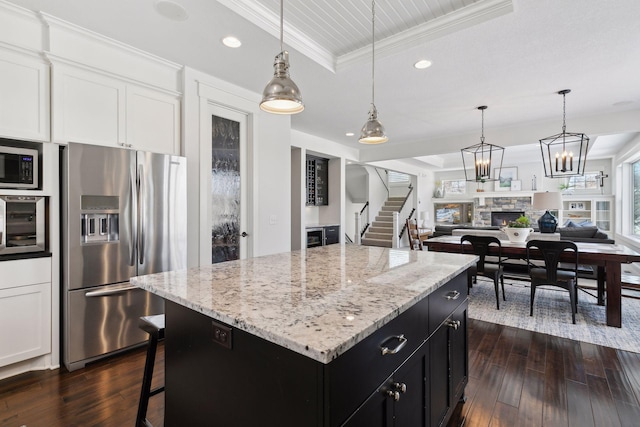 kitchen with stainless steel appliances, a raised ceiling, ornamental molding, a stone fireplace, and dark cabinetry
