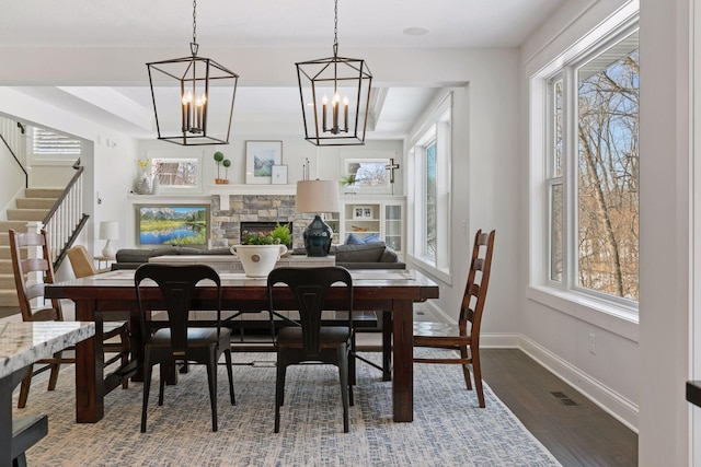 dining space featuring a fireplace, wood finished floors, visible vents, baseboards, and stairway