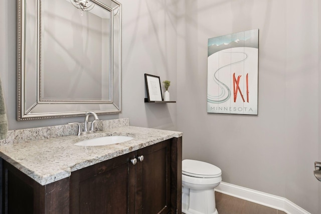 half bath with toilet, baseboards, wood finished floors, and vanity