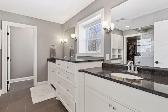 bathroom with visible vents, vanity, baseboards, and a spacious closet