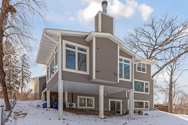 snow covered rear of property featuring ac unit, fence, and a chimney