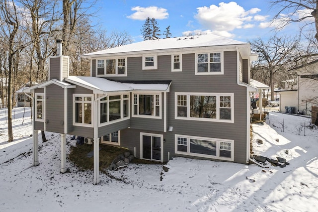 snow covered house with a chimney and a sunroom