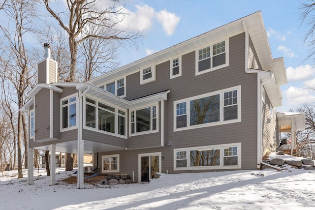 snow covered house with a sunroom and a chimney
