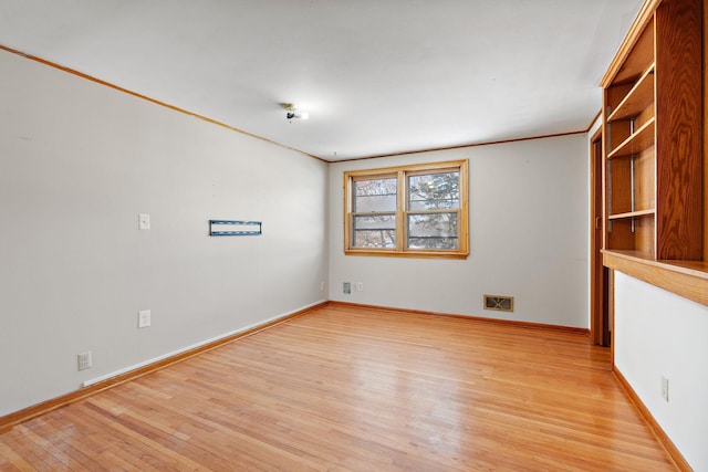 empty room featuring light wood-type flooring and ornamental molding