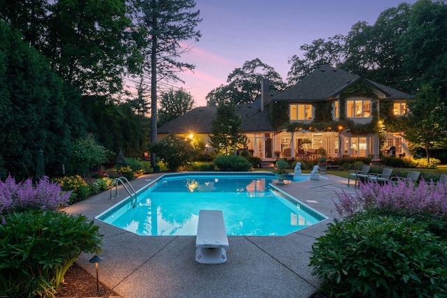 pool at dusk featuring a diving board and a patio area