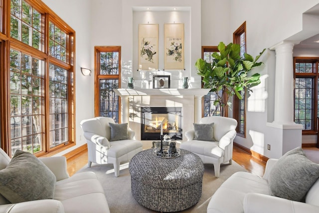 living room featuring plenty of natural light, light hardwood / wood-style flooring, ornate columns, and a towering ceiling