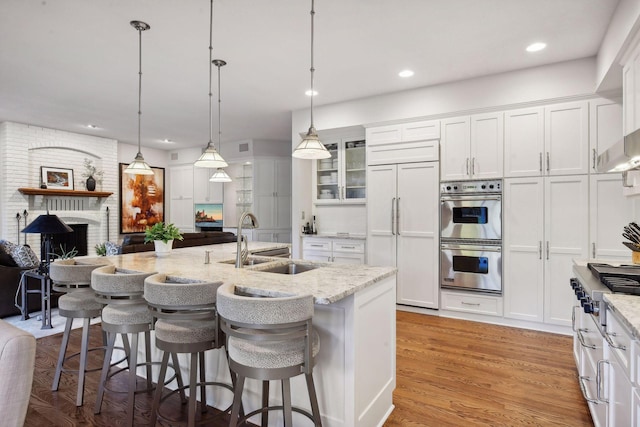 kitchen featuring paneled built in refrigerator, white cabinets, hanging light fixtures, and light stone counters