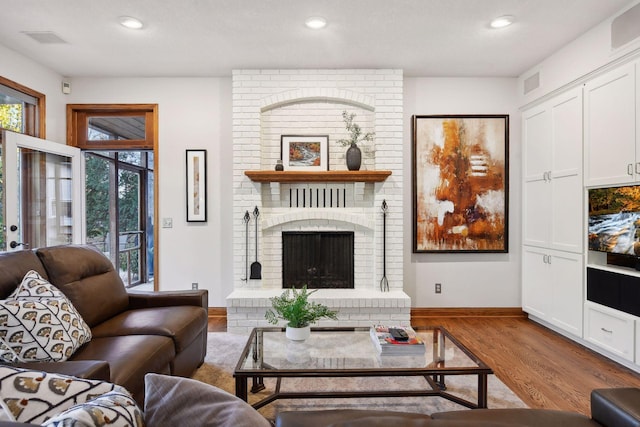 living room with a brick fireplace and light hardwood / wood-style flooring