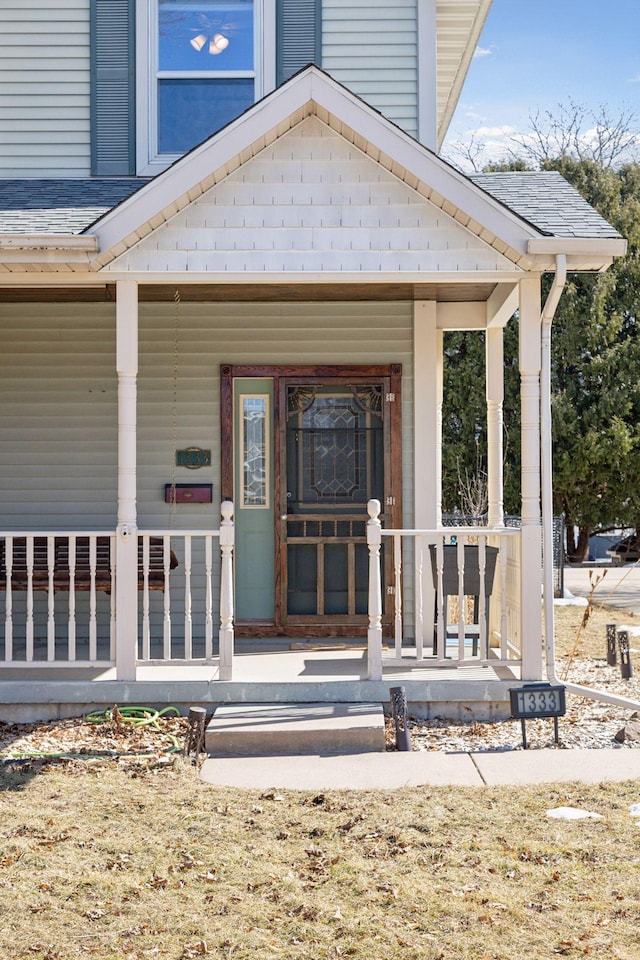 entrance to property with a porch and a shingled roof