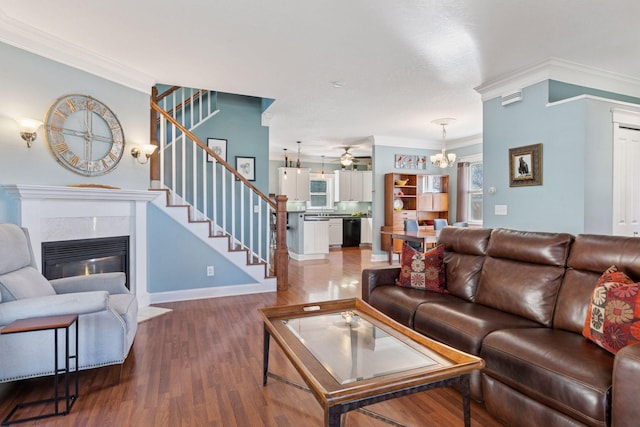 living room featuring ceiling fan with notable chandelier, wood finished floors, a fireplace, and ornamental molding