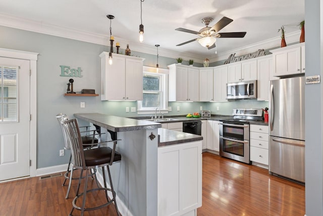 kitchen featuring dark countertops, a kitchen breakfast bar, appliances with stainless steel finishes, and a peninsula