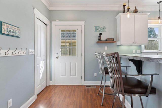 kitchen with visible vents, wood finished floors, white cabinets, crown molding, and baseboards