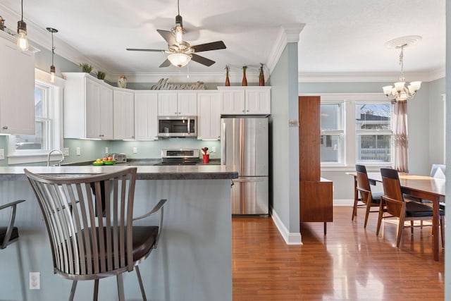 kitchen with a kitchen bar, ceiling fan with notable chandelier, dark countertops, appliances with stainless steel finishes, and dark wood-style flooring