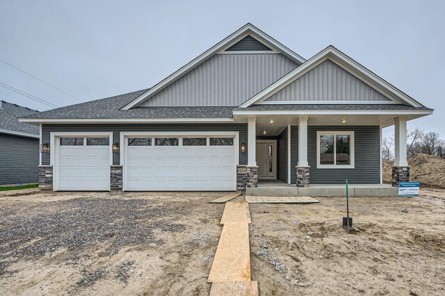 craftsman-style home with driveway, stone siding, a shingled roof, covered porch, and an attached garage